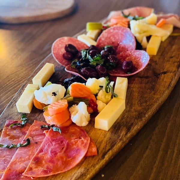 A wooden board with Italian charcuterie, cheeses, olives, and pickled vegetables.