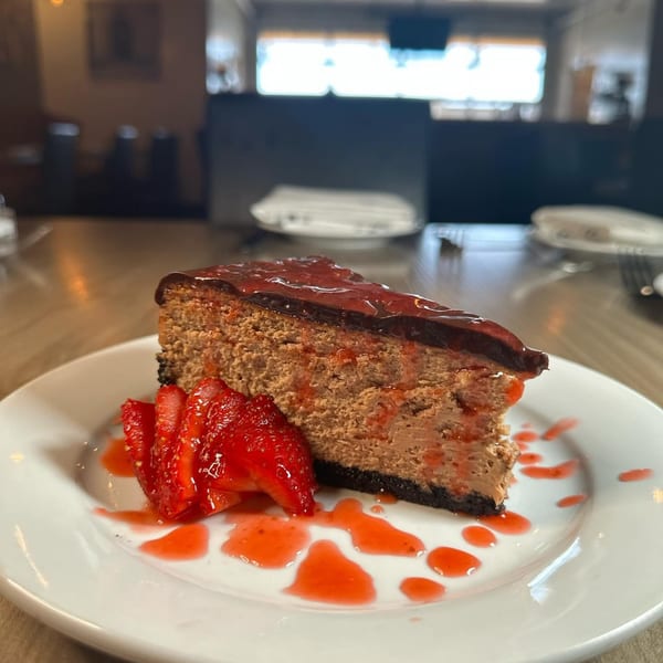 A slice of chocolate cheesecake with strawberry topping and fresh strawberries on a white plate.