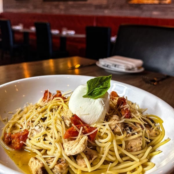 A bowl of spaghetti with chicken, sun-dried tomatoes, parmesan, and a dollop of burrata with basil.