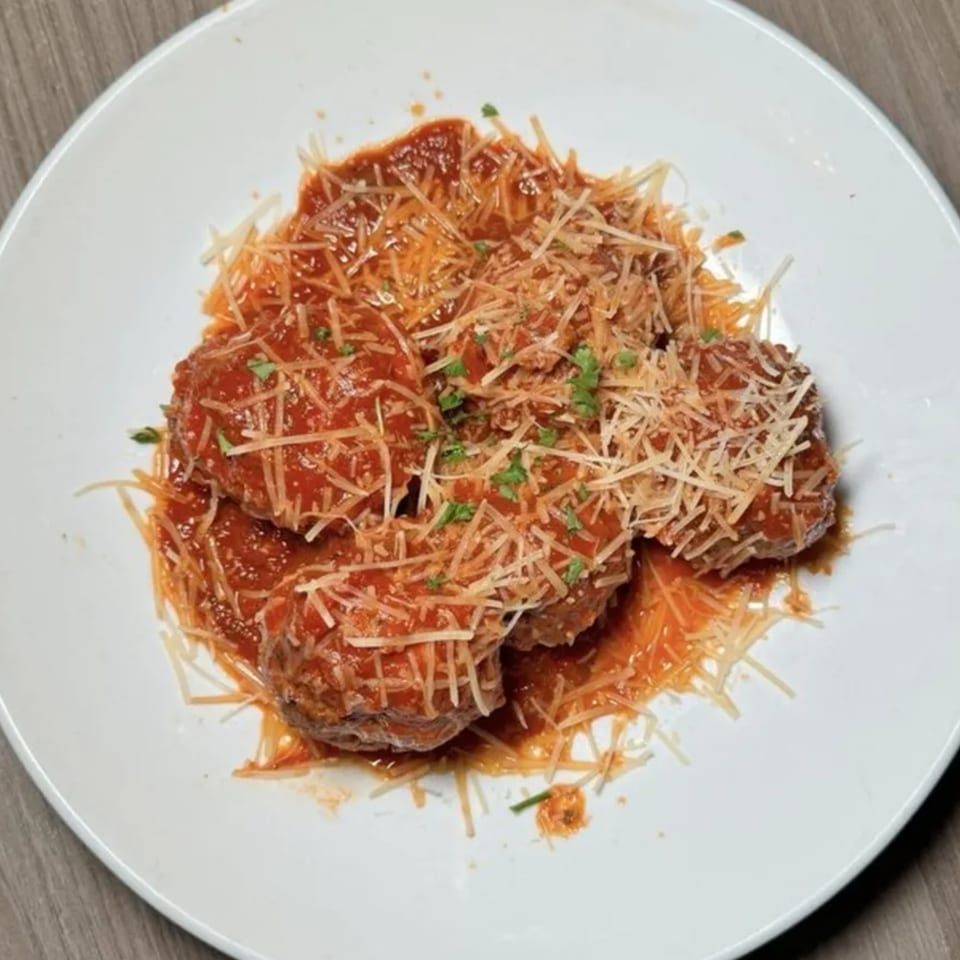 Four meatballs covered in red sauce, shredded Parmesan cheese, and green herbs on a white plate.