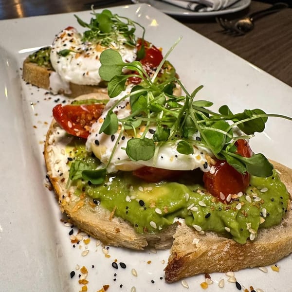 Two avocado toasts with poached eggs, cherry tomatoes, microgreens, and everything bagel seasoning.