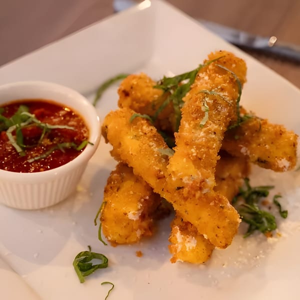 Golden-brown fried mozzarella sticks with marinara sauce and fresh basil on a white plate.